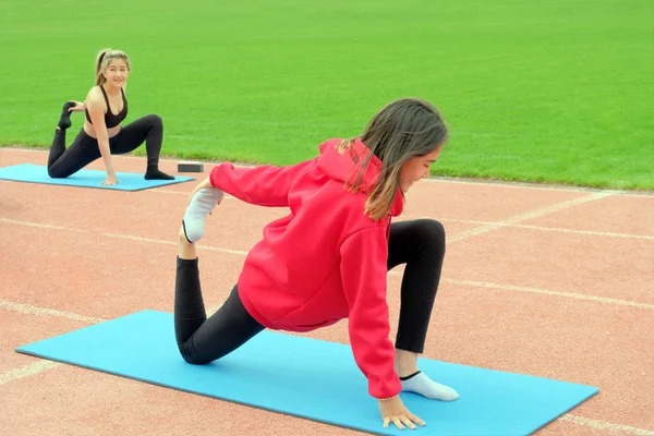 Due ragazze di etnia orientale sono impegnate in idoneità all'aria aperta. Esercizi di yoga Hatha per allungare e rafforzare i muscoli delle gambe. Uno stile di vita sano. Mattina allenamento di ginnastica . — Foto Stock