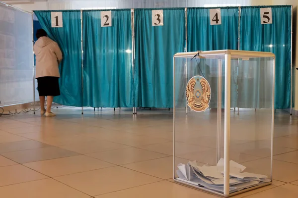 Qazaqstan, 9 Haziran 2019, seçimler. Bir kadın, tek bir oylama standına girer. Mavi. Oy sayma için Kazakistan amblemi ile şeffaf kutu. Close. Boşluk Kopyala.