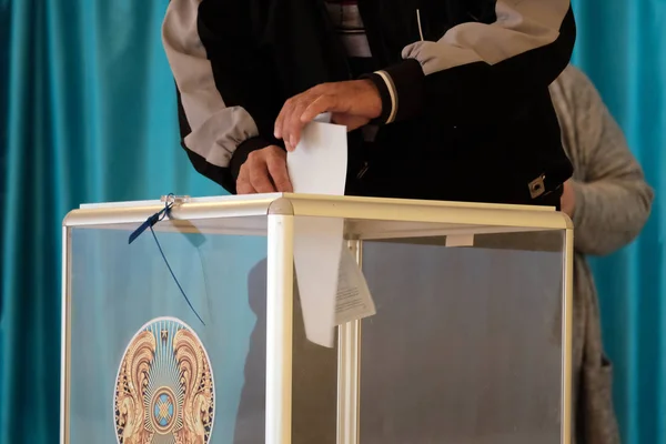 Ein Mann im Wahlsaal steckt den Stimmzettel in eine durchsichtige Schachtel mit dem Emblem Kasachstans. Hand in Hand. Kopierraum. qazaqstan, 9. Juni 2019, Wahlen, Abstimmung, — Stockfoto