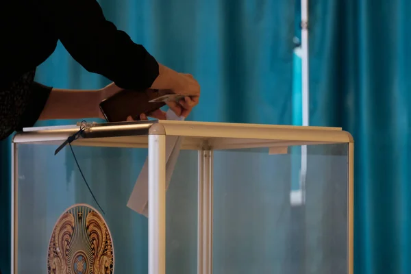 Kazakhstan, Qazaqstan, June 9, 2019, Elections, voting, A woman in the voting hall puts the ballot in a transparent box with the emblem of Kazakhstan. Hand close-up. Copy space. — Stock Photo, Image