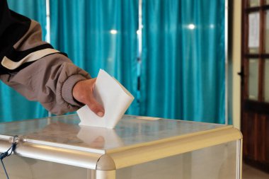 Polling station. Close-up. Male hand puts a ballot paper in a transparent box. Blue background. Banner. Nationwide voting, elections. clipart