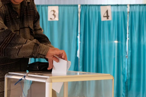 Polling station. Nationwide voting, elections. A man puts a paper sheet in a transparent box. Blue background. Cabins with numbers 3 and 4. — Stock Photo, Image