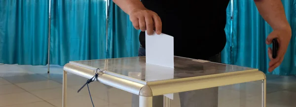 投票站全国投票,选举一个男人把一张纸放在一个透明的盒子里。蓝色背景。旗帜. — 图库照片