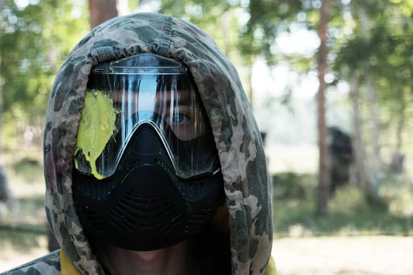 Paintball. The defeat of the player in the head. Portrait of a guy in a camouflage hood and a protective mask with a yellow blot on the glass. Sports lifestyle, entertainment and team war games. — Stock Photo, Image