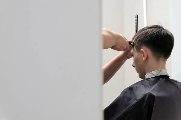 Um jovem no corte de cabelo da barbearia. A tirar fotos da esquina. Espaço para cópia. Fundo branco. Adolescente em um salão de beleza . — Fotografia de Stock