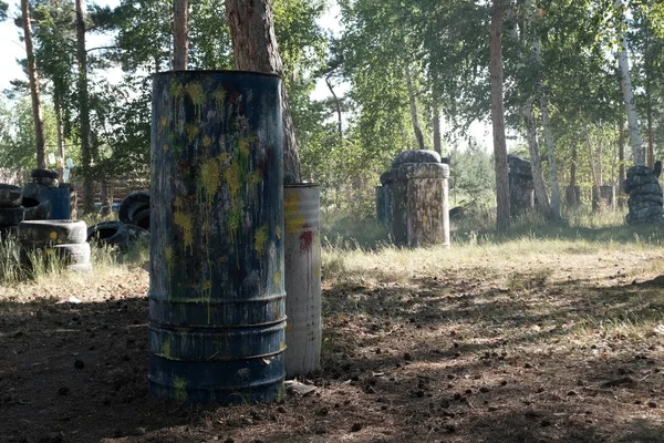 Çok renkli lekeler ve paintball silah çekim lekeleri ile ön planda Demir varil. Arabadan ve ağaçlardan eski lastikler. Arka plan açık havada popüler bir savaş oyunu reklamını yapmak.