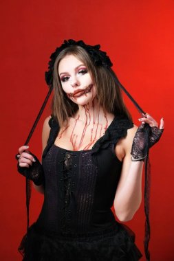 Cadılar Bayramı parti kıyafeti. All Saints Günü için makyaj ve siyah giysiler. Kırmızı bir arka plan üzerinde korkutucu bir görüntü güzel kız.