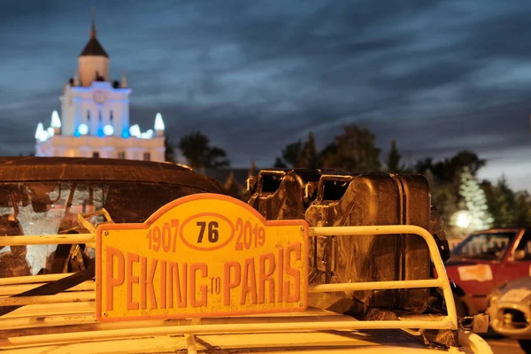 Kazakhstan, Kostanay, 19-06-19, Part of a retro car with gas canisters against the background of the city clock tower. Member of the historic rally number 76. Peking to Paris. Rally. Evening lighting. — Stock Photo, Image