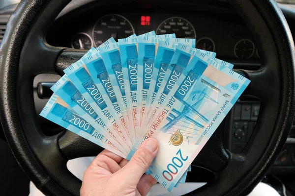 Arabadaki direksiyonun arka planında erkek elinde bir Rus parası. 20.000 ruble. Kazanç veya rüşvet, sigorta veya kredi, yatırım veya Rusya'da bir araba satan kavramı.