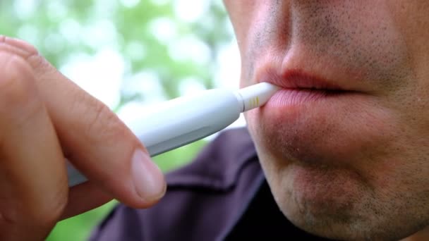 Il fume à l'air libre. Gros plan d'une bouche masculine d'un jeune homme avec une cigarette électronique. Inhalation de fumée blanche avec nicotine . — Video