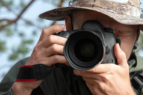 El fotógrafo viajero con sombrero mira a la lente de la cámara. Estilo de vida, historia fotográfica, fotografía natural. Viajes y turismo . — Foto de Stock