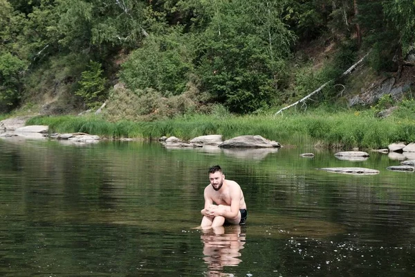Magányos nedves barna fickó az úszónadrág fagyasztott ül a vízen a folyón, vagy egy hegyi tó, és szomorúan néz a távolba. Fogalmát magány, elveszett, várva segítséget. — Stock Fotó