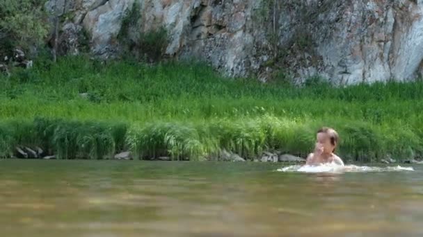 Oğlu babasının omuzlarında oturuyor. Babam çocuğu suya atar. Dağ nehrinde aile eğlencesi. Tatilde banyo ve yüzme. Kamp. — Stok video