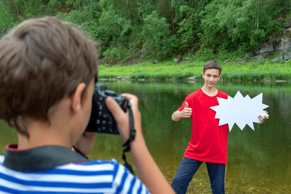 一个穿着条纹T恤的男孩拍摄了一名穿着红色T恤的少年的照片,他举着一个白色标志,竖起大拇指。概念折扣、季节性销售、旅游广告和儿童旅游线路 — 图库照片