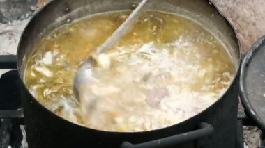 Güzel lezzetli çorba ateşte büyük bir tencerede kaynar. Kamp mutfağı. Bir kepçe ile bir el malzemeleri karıştırır. Turistler için doğada yemek pişirmek. Yürüyüş yolcuları için yiyecek. Close.