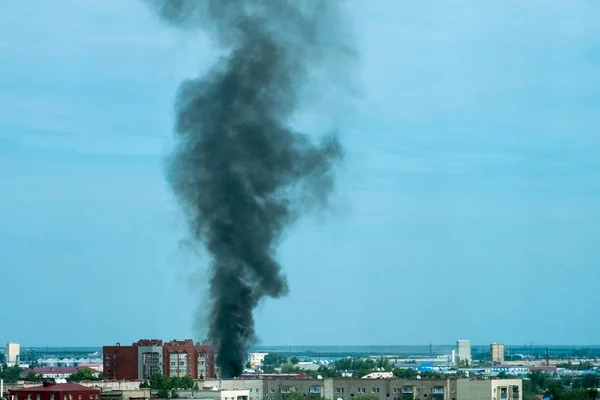 Plume of black smoke from a fire above city at sunset. Technogenic accident