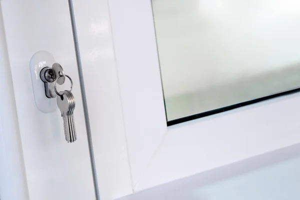 New keys are inserted into the door lock next to the window. Opening or closing a white plastic door. The concept of forgetfulness and distraction of the landlord or the acquisition of new housing. — Stock Photo, Image
