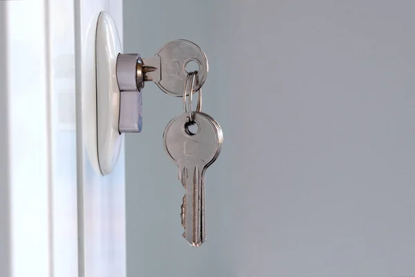 New keys are inserted into the mortise lock. Opening or closing a white plastic door. The concept of forgetfulness and distraction of the landlord or the acquisition of new housing. Copy space. — Stock Photo, Image