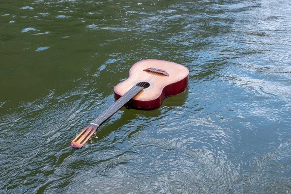 Музыка не тонет. Акустическая гитара плавает в реке, озере или другом водоёме. Концепция кораблекрушения, наводнения, трагедия музыкантов в природе. Копирование пространства . — стоковое фото