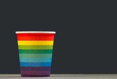 Kağıt bardak beyaz bir masa, gri arka plan üzerinde bir gökkuşağı olarak boyanmış. Renklendirme Lgbt sembol kavramı veya kafede kutlama içkisi. Kopyalama alanını yalıtma.