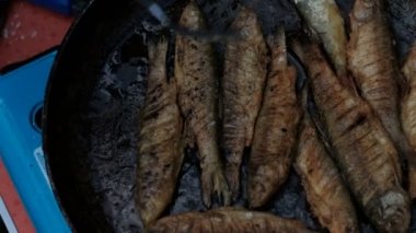 Un serpilir küçük balık sıcak yağda bir tavada kızartılır. Erkek el bir çatal ile balık çevirir. Balık tutarken yemek pişirmek. Close.