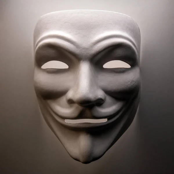 Šablona bílé masky podobná symbolu skupiny hackerů nazvané Anonymous. Close-up. Natáčíme předmět v tmavém klíči. Čtvercový rámeček. — Stock fotografie