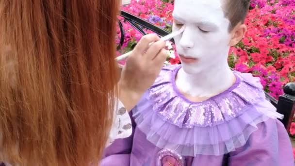 Kazajstán, Kostanay, 19-08-16La mano femenina de un artista callejero con un pincel pinta la cara de un adolescente con pintura blanca. Crear una imagen de un payaso con dientes o mimo. Maquillaje de Halloween o celebración del Día de Todos los Santos . — Vídeo de stock