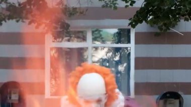 Makyaj ve korkunç bir palyaço Pennywise gibi bir kostüm ile bir cosplayer ankesörlü ve pencereli bir binanın arka planda yangın görünür. Cadılar Bayramı kutlama veya All Saints Günü maskeli.