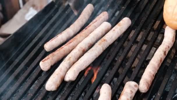Az ember keze segítségével a fogó, hogy egy hotdog a kenyér roll. Közeli. Egy utcai séf, fekete kesztyű felmelegíti kolbász egy grill. Főzés a szén. Gyorsétterem.