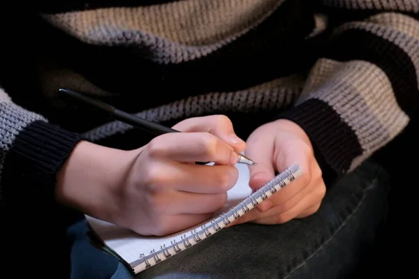 Quaderno e penna nelle mani di uno scrittore adolescente. Un tizio con un maglione scrive qualcosa in un quaderno per appunti. Il concetto di imparare, prendere appunti, scrivere poesie. Primo piano . — Foto Stock