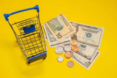 Süpermarket alışveriş arabasının yanında dolar ve sent. Sarı arka plan. Alışveriş kavramı, indirimler, online alışveriş, tüketici yeteneği veya black friday.