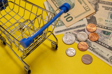 Bir süpermarkette bir alışveriş arabası yanında Amerikan doları ve sent yakın çekim. Sarı arka plan. Alışveriş kavramı, indirimler, online alışveriş, tüketici yeteneği veya black friday.