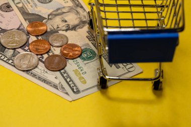 Bir süpermarkette bir alışveriş arabası yanında Amerikan doları ve sent yakın çekim. Alışveriş kavramı, indirimler, online alışveriş, tüketici yeteneği veya black friday. Sarı arka plan.