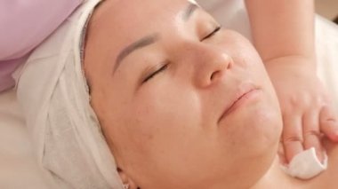 Bir güzellik salonunda cilt temizliği için kozmetik prosedür. Güzellik uzmanı Asyalı kadının yüzünü pamuk pedlerle siliyor. Gençleştirme, güzellik ve sağlık. Doğu tıbbı.