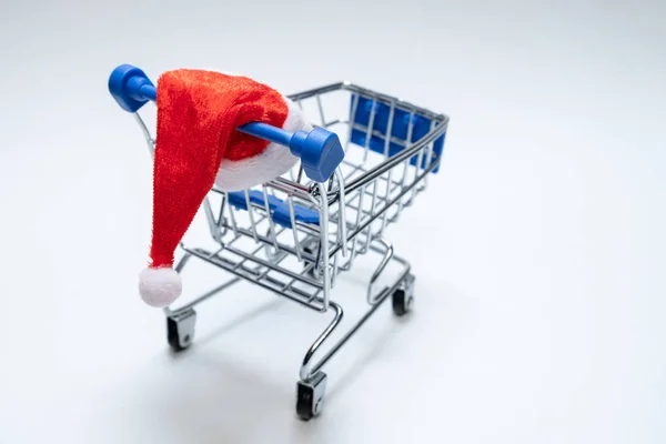 산타 모자와 쇼핑 바구니. 흰색 배경에 금속 트롤리. 공간을 복사합니다. 새해와 크리스마스 온라인 구매 및 판매의 개념. — 스톡 사진