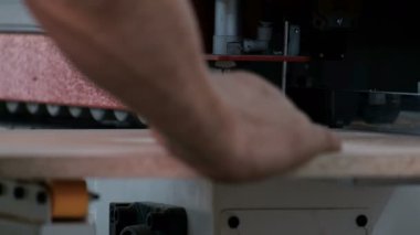 Bir adam ahşap parçaları kenar için bir makine üzerinde çalışır. Close. Mobilya imalatı. Kılavuz silindirler üzerinde yonga levha hareketinin başlangıcı. Bir iş makinesinin gerçek sesi.
