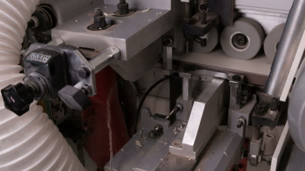 Close-up van de achterzijde van de rand banding machine. Automatisch lijmen, trimmen van bruine PVC-randen en afschuinen in meubelproductie. Een detail van witte spaanplaat rollen op wielen. — Stockvideo