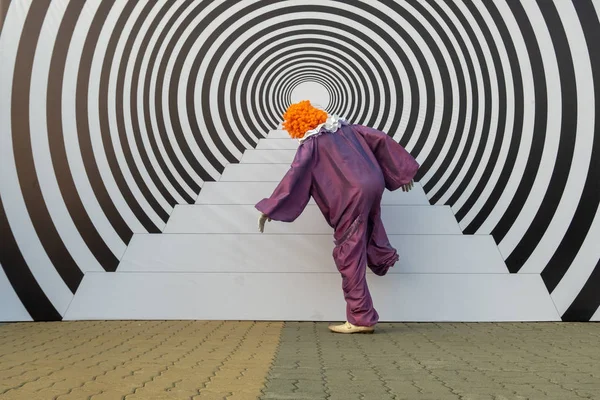 Muž v klaunském kostýmu předstírá, že šplhá po schodech. 3D obraz na ulici ve formě schodů a soustředné kružnice. Hypnotický efekt a optická iluze. — Stock fotografie