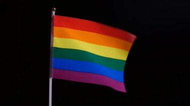 Gökkuşağı renklerinde bir gurur bayrağı rüzgarda sallar. Siyah bir arka plan üzerinde LGBT bayrağı. Aynı cinsiyetten insanlar arasında bağımsızlık ve sevgisembolü. Düzgün yakınlaştırma ve uzaklaştırma. Cinsel azınlıklar kavramı.