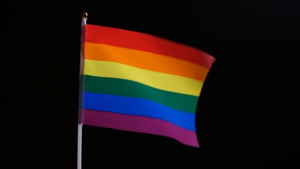 虹色のプライドフラッグが風に揺れる 黒い背景にLgbtフラグ 同性同士の自立と愛の象徴 スムーズなズームイン ズームアウト 性的マイノリティの概念 — ストック動画