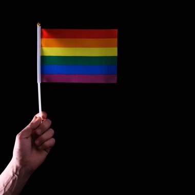 Bir erkek elinde LGBT gökkuşağı gurur bayrağı. Siyah bir arka plan üzerinde izole edilmiş. Kare, kopya alanı. Aydınlatma modelleme. Aynı cinsiyetten insanların özgürlüğünün ve sevgisinin sembolü. Cinsel azınlıklar kavramı.