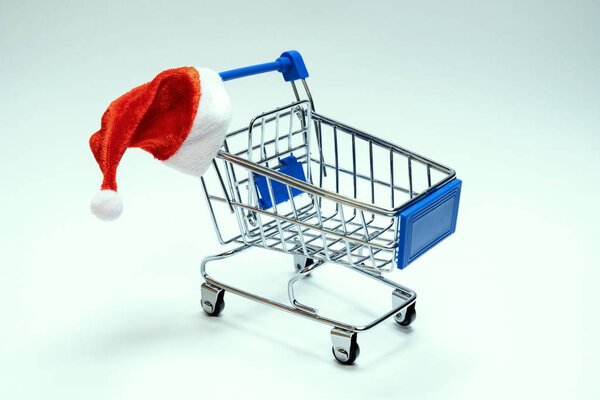 Santa Claus hat on a shopping trolley on a white background. Christmas and New Year discount concept, online, black friday and holiday sale.