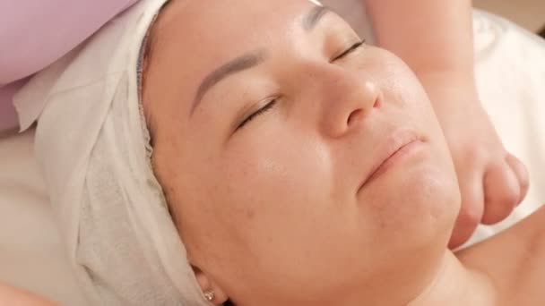 一个亚洲女孩在美容和健康沙龙的清洁和振兴皮肤的程序 麻醉师用棉垫擦拭女性脸的特写 — 图库视频影像