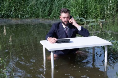 Bataklıkta bir ofis çalışanı. Takım elbiseli, kravatlı, sakallı genç bir adam. Beyaz bir masada pantolonsuz, resmi ya da işadamı elinde bir telefon ahizesi tutuyor..