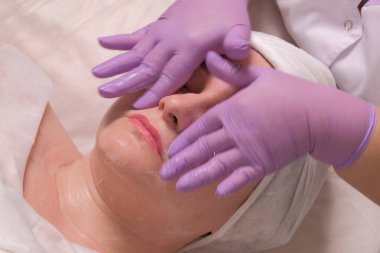 Güzellik salonunda yaşlanma karşıtı bir kadın. Bir kozmetoloji merkezinde yüz temizleme. Güzellik uzmanının sabun sürerken yaptığı hareketler..