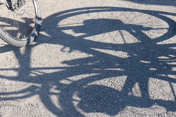 Radfahren. Schatten und Rad eines Fahrrades auf dem Bürgersteig. Abstrakter Hintergrund. Konzept und Förderung eines gesunden Lebensstils in der Bevölkerung. Sportereignis Radtour. — Stockfoto