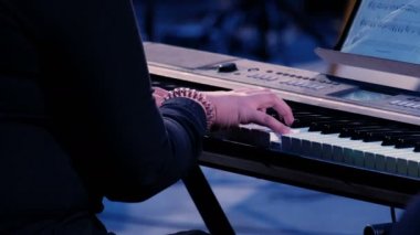 Woman hands playing electric piano under colorful stage lighting, close-up. Musician girl perform a composition on a keyboard music workstation on a party night.