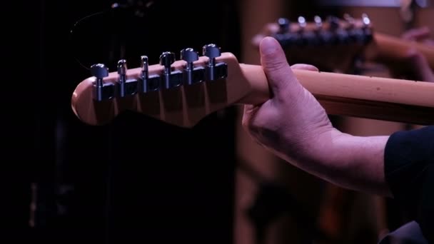 Gitarrist. Närbild. Den vänstra manliga handen klämmer åt strängarna på en sexsträngad gitarrs skrivtavla. Bakåt. Musikkonsert eller -fest. — Stockvideo