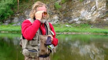 Sinek avı. Noel Baba 'ya benzeyen sakallı bir adam gözlüklerini ayarlıyor ve bir şeyler söylüyor. Kırmızı elbiseli deneyimli bir balıkçı suyun içinde duruyor. Dağ nehri. Kamp, spor balıkçılığı