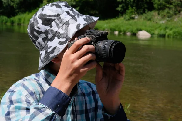 Странный фотограф на природе. Молодой человек в рубашке и шляпе смотрит сквозь глазок расплавленной камеры SLR. Тропическая жара испортила камеру. . — стоковое фото